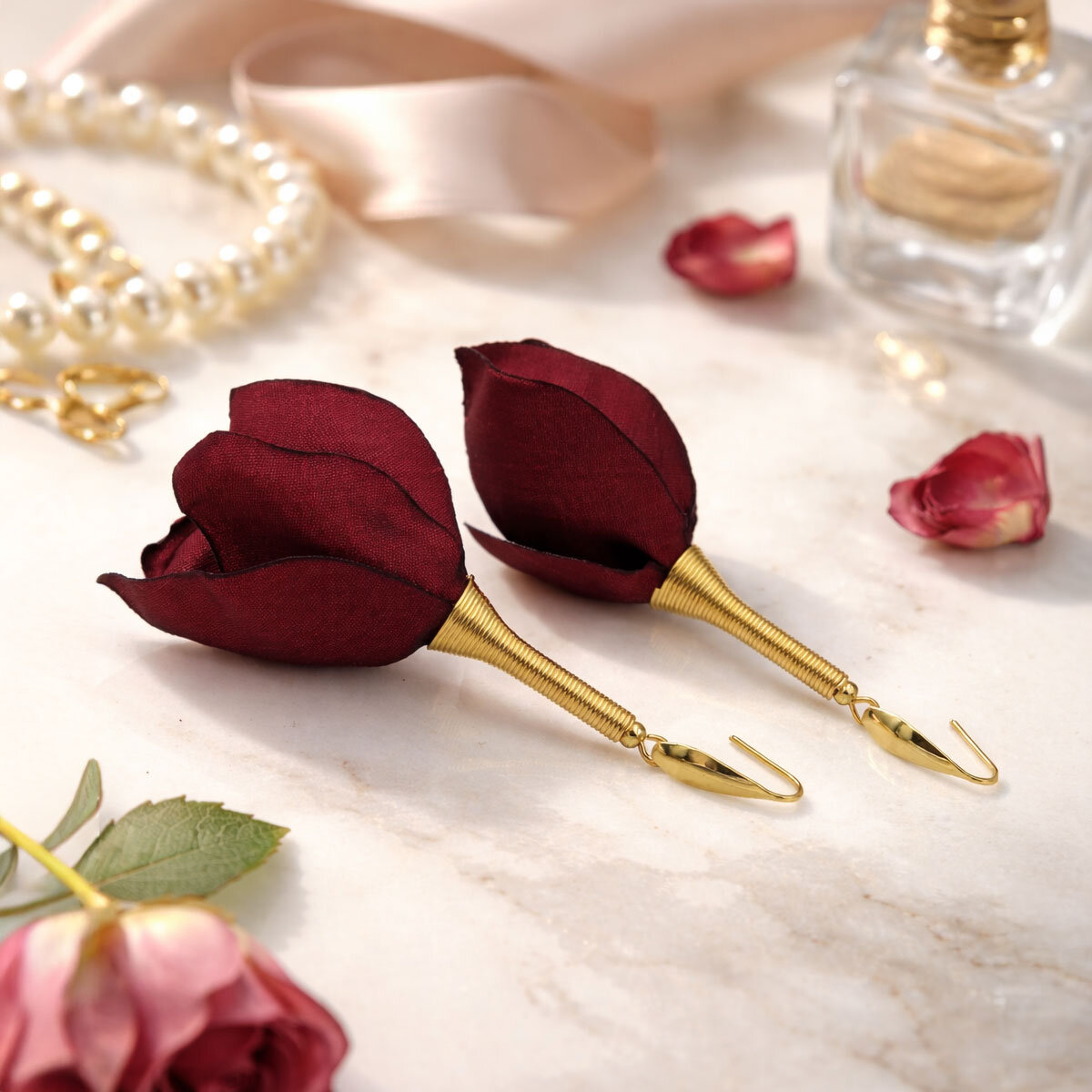 Długie, wiszące kolczyki w kształcie kwiatów uformowanych z asymetrycznych płatków tkaniny w kolorze ciemnego bordo