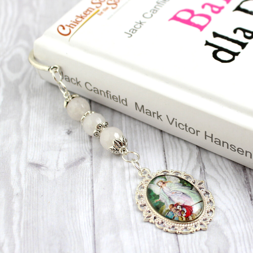 Srebrna zakładka do książki zdobiona motywem roślinnym, z zawieszką z kamieni białego jadeitu i wizerunkiem Anioła Stróża z dziećmi pod szklanym kaboszonem