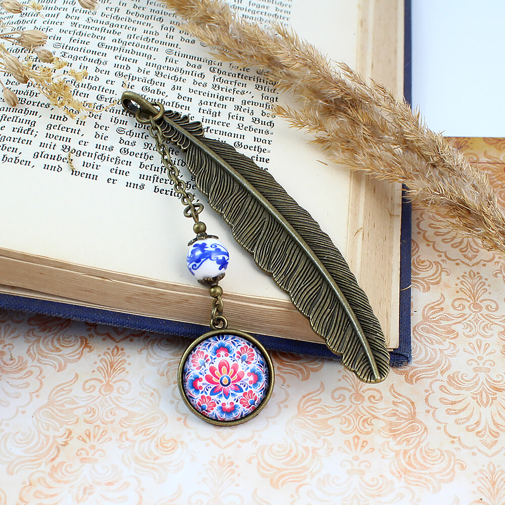 Zakładka do książki z antycznego brązu z ozdobnym, ceramicznym koralikiem i barwnym wzorem ludowych kwiatów pod szklanym kaboszonem.