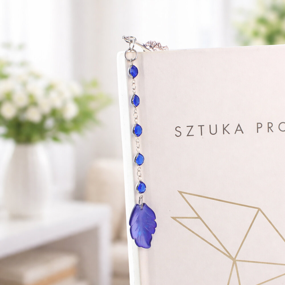 Cienka i lekka metalowa zakładka do książki w kształcie pióra, zdobiona wiszącą zawieszką z szafirowych szklanych kryształków i niebieskiego akrylowego listka, w ozdobnym pudełku. Cienka i lekka metalowa zakładka do książki w kształcie pióra, zdobiona wiszącą zawieszką z szafirowych szklanych kryształków i niebieskiego akrylowego listka, w ozdobnym pudełku.