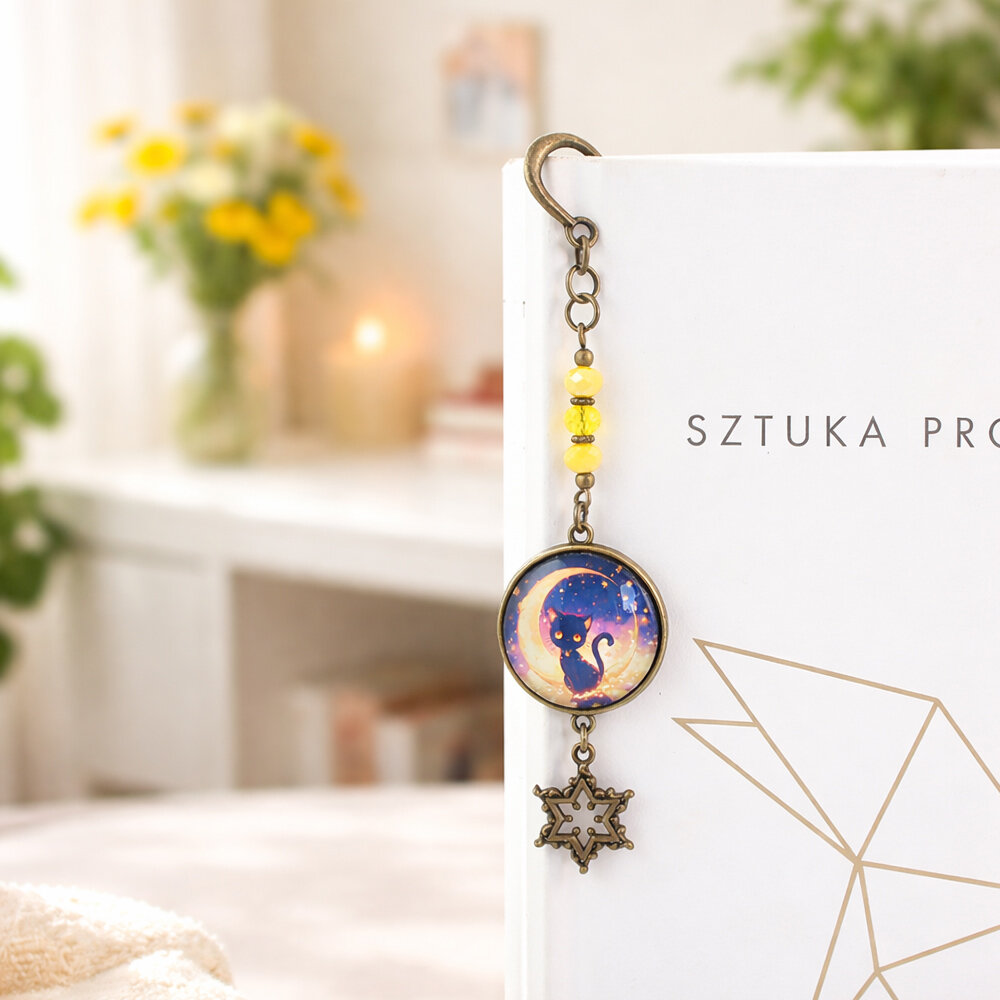 Zakładka do książki w kolorze antycznego brązu w kształcie pióra, z żółtymi kryształkami, zawieszką gwiazdką i wizerunkiem czarnego kota na tle księżyca pod szklanym kaboszonem