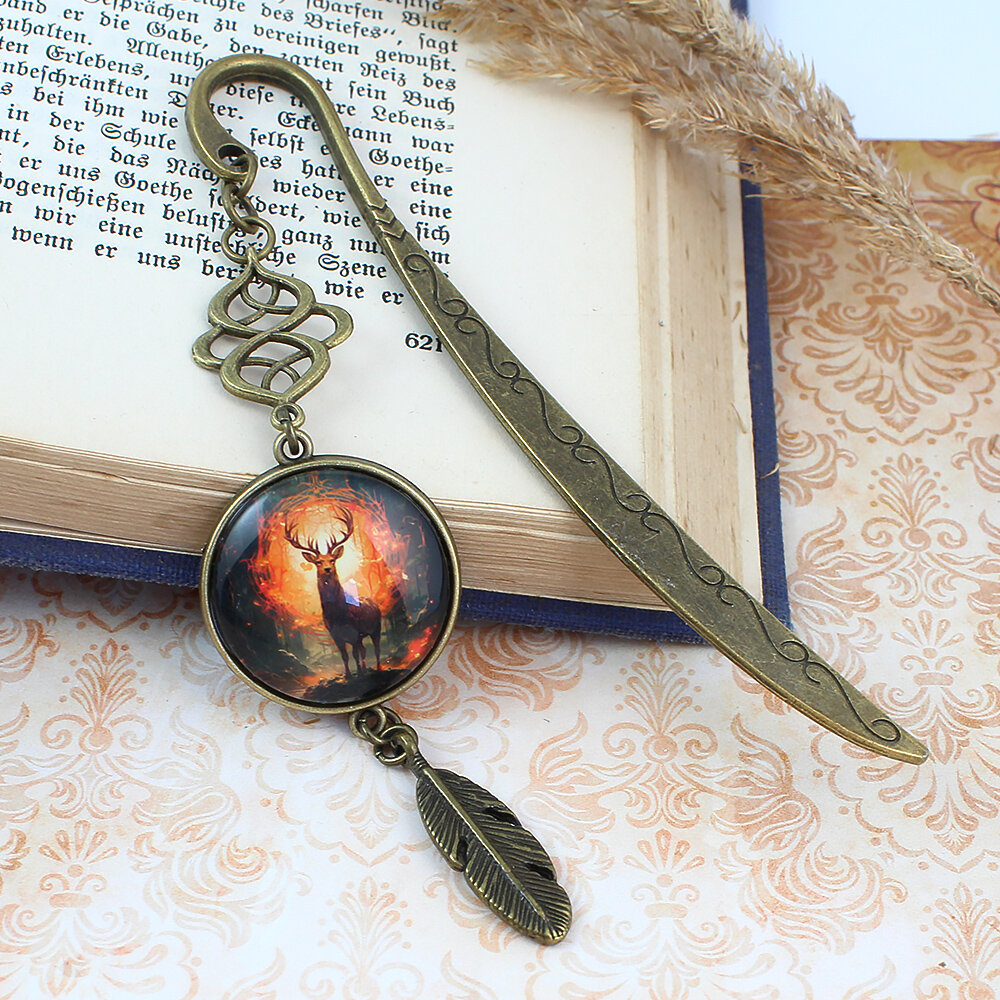 Zakładka do książki z antycznego brązu z ozdobnym falistym trzonem, zawieszką z piórkiem i ilustracją jelenia w ognistym lesie pod kaboszonem.