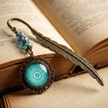 Zakładka do książki piórko w kolorze antycznego brązu z turkusowymi kryształkami i zawieszką z mandalą pod szklanym kaboszonem Zakładka do książki piórko w kolorze antycznego brązu z turkusowymi kryształkami i zawieszką z mandalą pod szklanym kaboszonem
