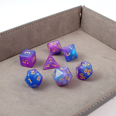 Zestaw brokatowych kości RPG Astro Dust w kolorach niebieskim i fioletowym ze złotymi cyframi.