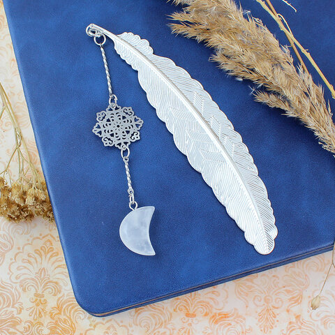 Cienka srebrna zakładka do książki pióro z zawieszką z kryształu górskiego w kształcie księżyca i ażurową rozetką w ozdobnym pudełku.