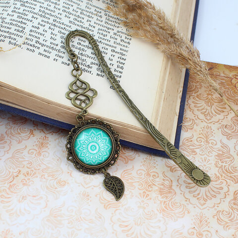 Zakładka do książki z antycznego brązu o falistym trzonie, z ozdobnym koralikiem i uspokajającą, turkusową mandalą pod szklanym kaboszonem. Zakładka do książki z antycznego brązu o falistym trzonie, z ozdobnym koralikiem i uspokajającą, turkusową mandalą pod szklanym kaboszonem.