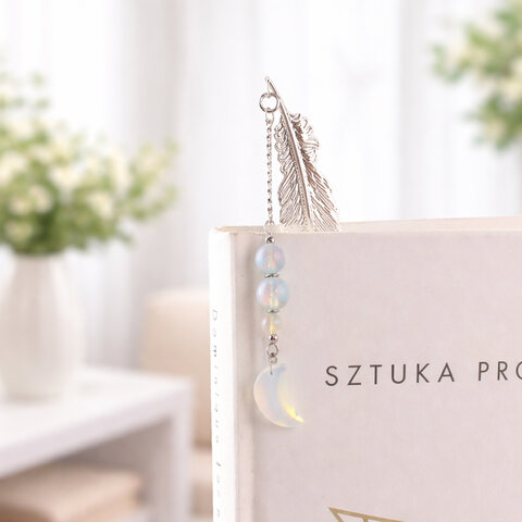 Subtelna metalowa zakładka do książki w formie piórka, zdobiona wiszącą zawieszką z opalitu w kształcie księżyca, umieszczona w pudełku prezentowym. Subtelna metalowa zakładka do książki w formie piórka, zdobiona wiszącą zawieszką z opalitu w kształcie księżyca, umieszczona w pudełku prezentowym.