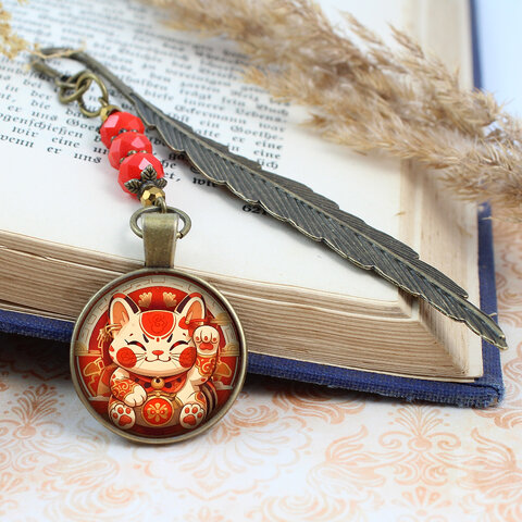 Zakładka do książki z antycznego brązu w kształcie pióra, z czerwonymi kryształkami i grafiką radosnego kota Maneki Neko pod szklanym kaboszonem