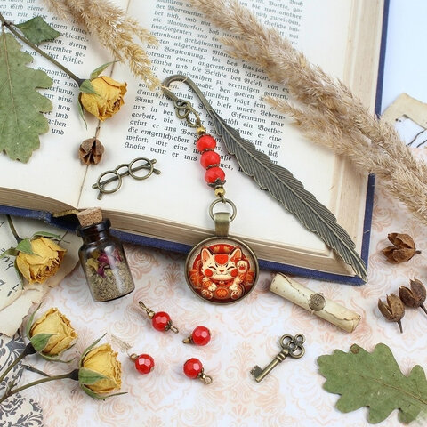 Zakładka do książki z antycznego brązu w kształcie pióra, z czerwonymi kryształkami i grafiką radosnego kota Maneki Neko pod szklanym kaboszonem