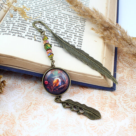 Zakładka do książki z antycznego brązu z szklanym kaboszonem w oprawie zdobionej kryształkami, przedstawiającym ryciny w stylu vintage z sikorą bogatką i zawieszką w kształcie piórka.