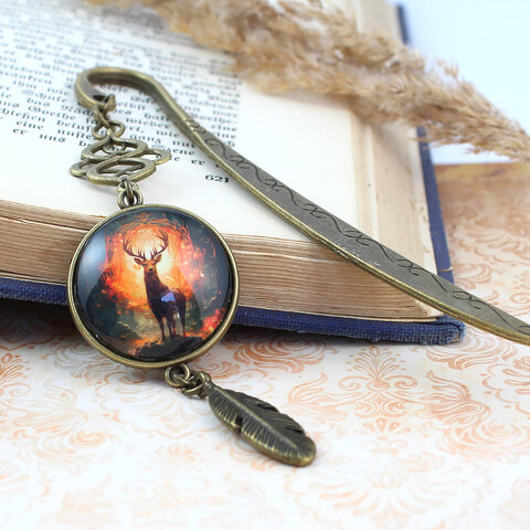 Zakładka do książki z antycznego brązu z ozdobnym falistym trzonem, zawieszką z piórkiem i ilustracją jelenia w ognistym lesie pod kaboszonem 