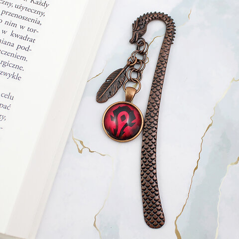 Metalowa zakładka do książki w kształcie smoka w kolorze oksydowanej miedzi z czerwoną grafiką z symbolem Hordy z World of Warcraft pod szklanym szkiełkiem oraz małą zawieszką w kształcie piórka.