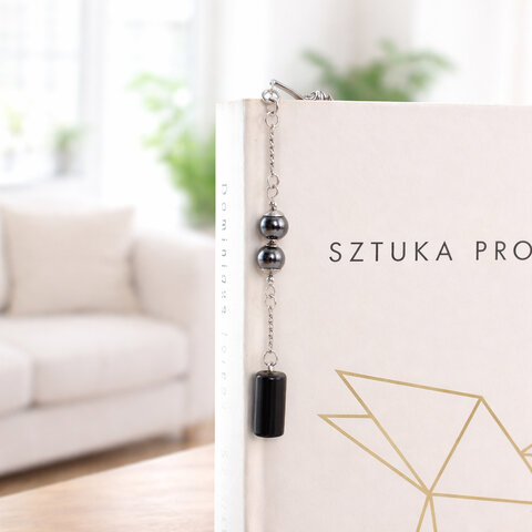 Cienka metalowa zakładka do książki pióro w kolorze grafitowym z zawieszką z czarnego onyksu i kulistego hematytu, w czarnym pudełku.